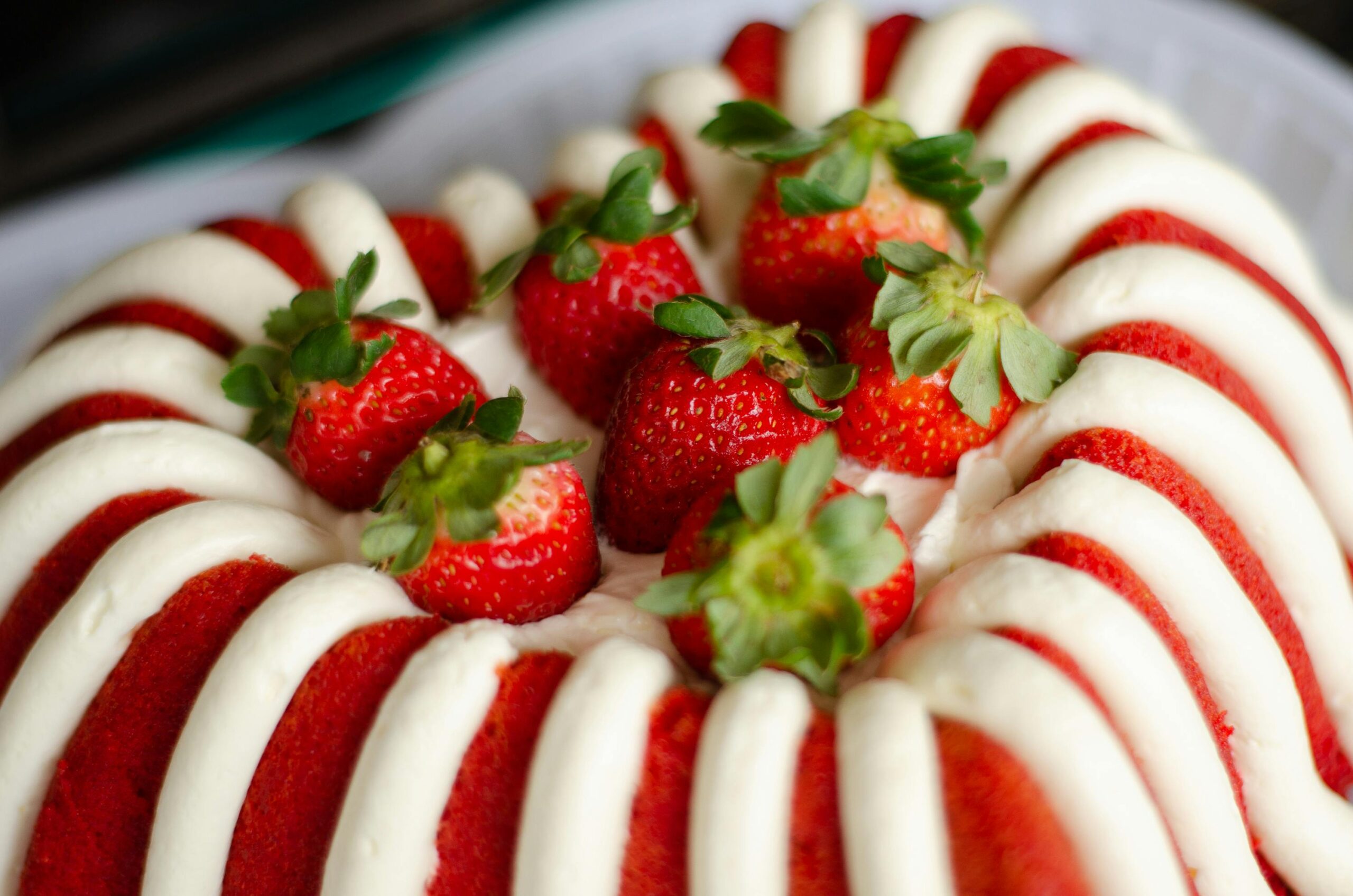 Close-up of a red and white striped bundt cake topped with fresh strawberries, perfect for sweet indulgence.